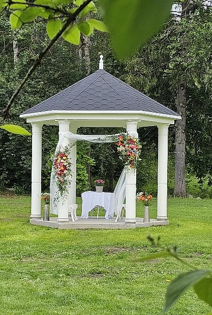 Hvit pavilijong i grønn hage, pyntet til bryllup med slør og blomster